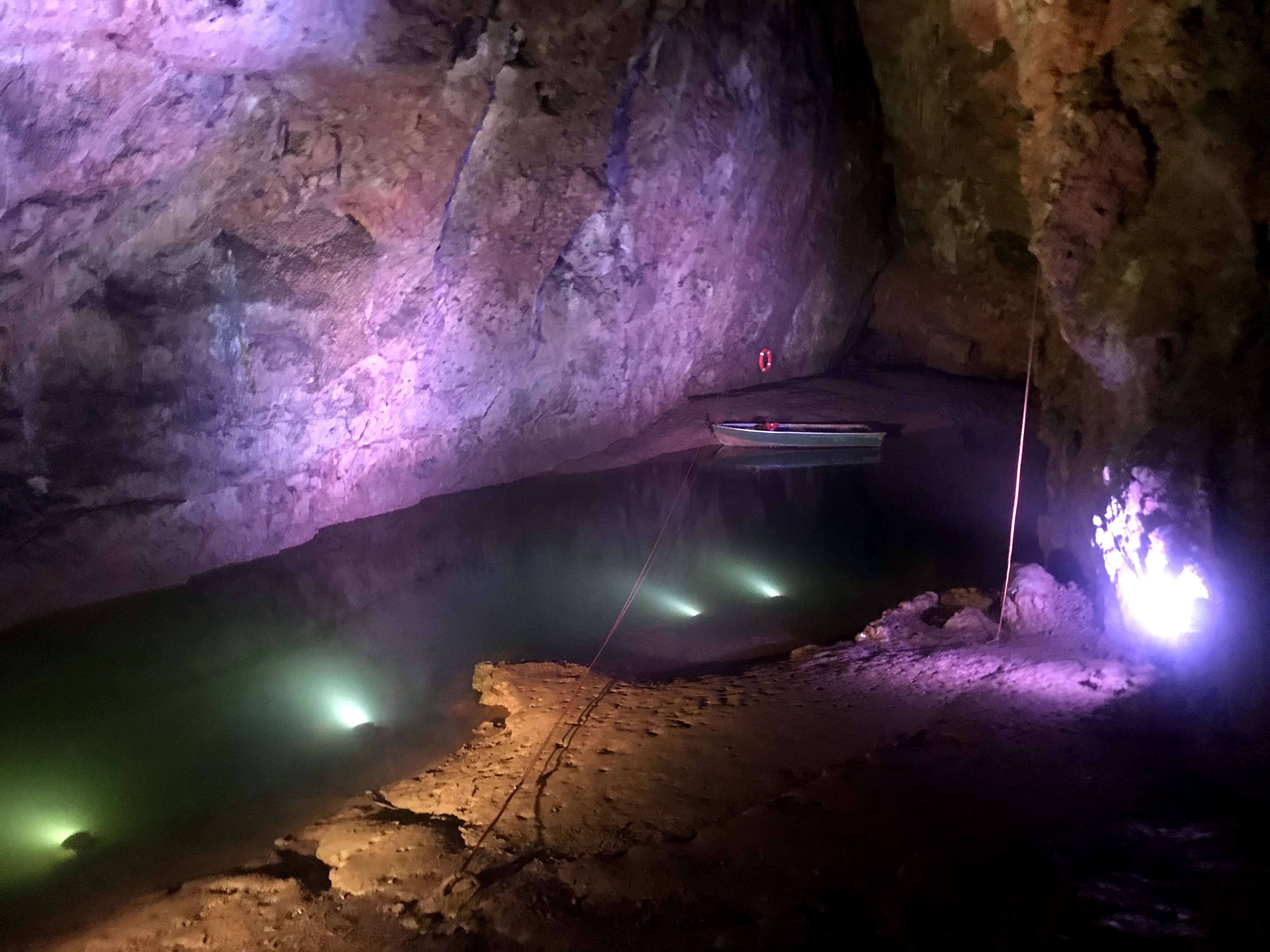 A pond in a cave with a small boat and being lit with purple lighting.